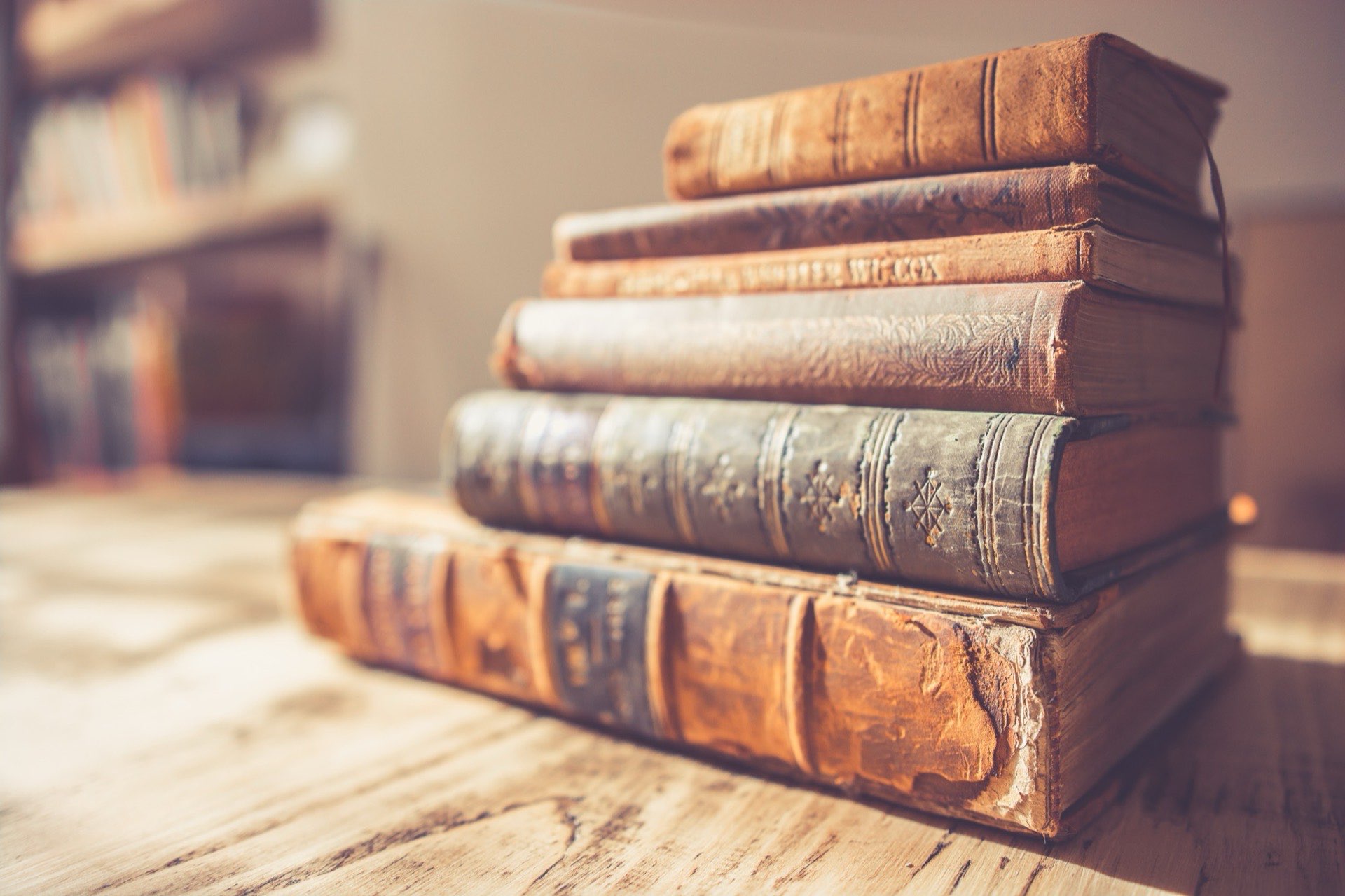 A stack of old leather-bound books on a sunlit wooden table